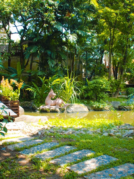 Lush garden with a pond and sculpture at Erawan Museum, Thailand.