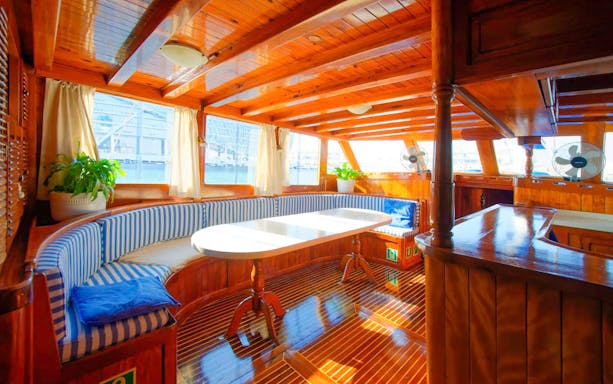 Interior of a wooden boat with striped seating and a table on the Yas Marina Boat Tour.
