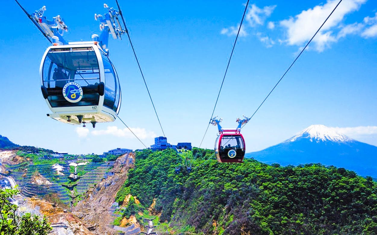 Ropeway over green hills with Mt. Fuji in the background, part of the Mt. Fuji & Hakone Tour.
