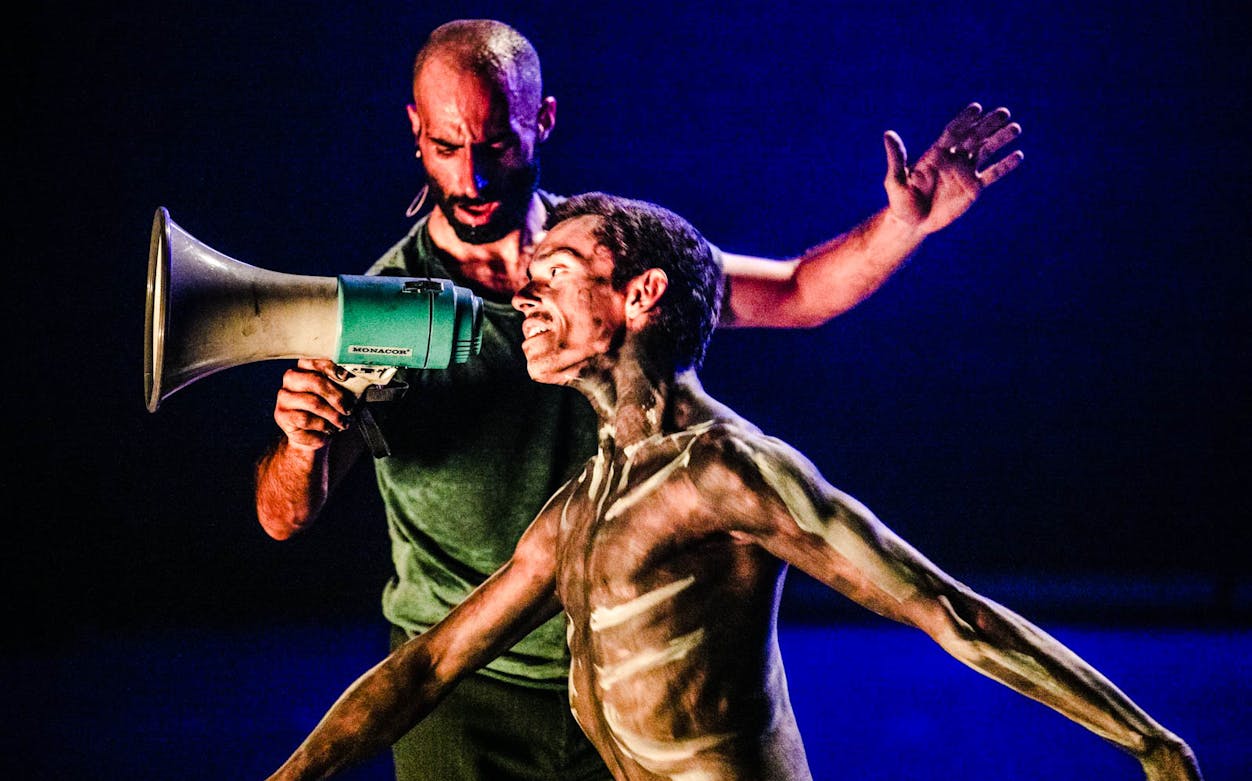 Man with megaphone directing a painted performer in a theatrical scene.