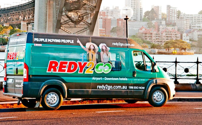 Sydney airport shuttle van near Harbour Bridge, offering transport to city hotels.