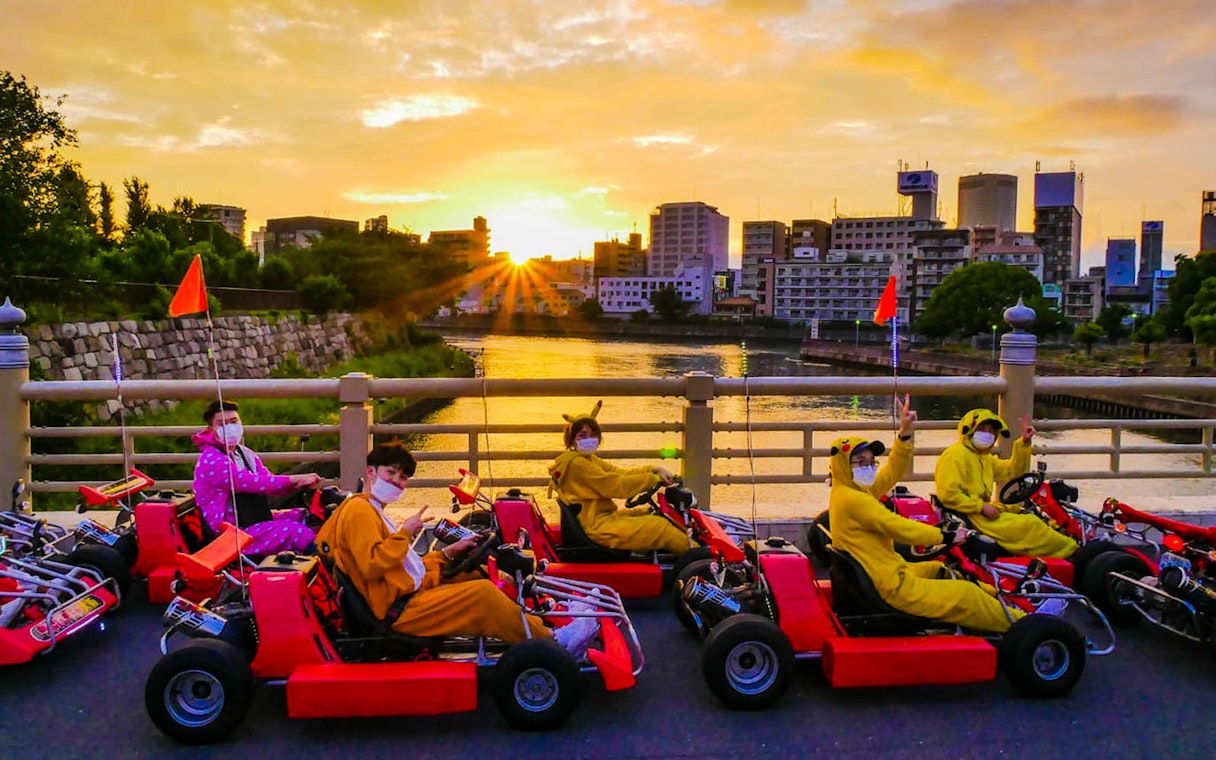 Go-kart riders in costumes on a bridge during sunset, Akiba Kart Osaka Street Go Kart Experience.