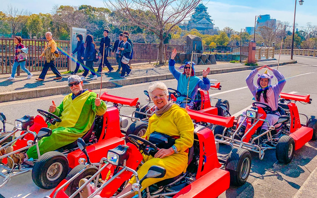 Go-kart riders in costumes on Osaka street with Osaka Castle in the background.
