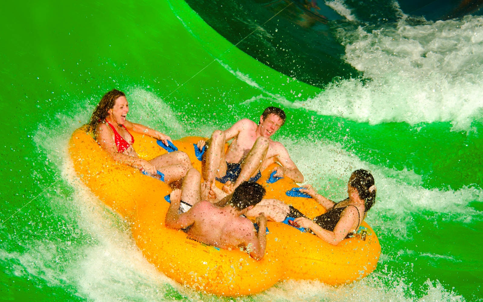 Group enjoying a water slide on a yellow raft at Wet 'n' Wild park.