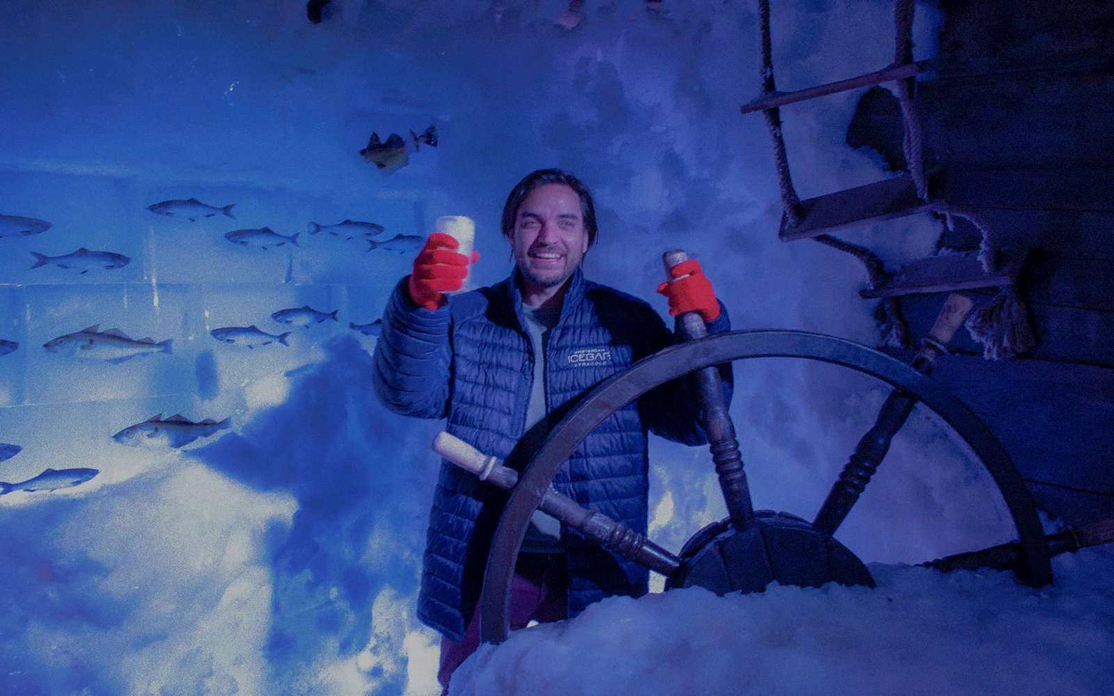 Man enjoying drinks at Amsterdam Icebar with ship wheel and ice wall.