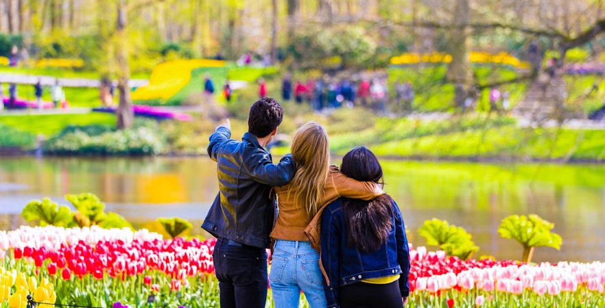 Visitors enjoying tulip gardens at Keukenhof, Netherlands, with a scenic pond view.