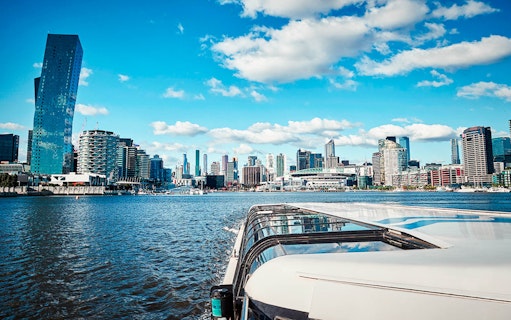 Cruise boat on river with city skyline and modern buildings in the background.