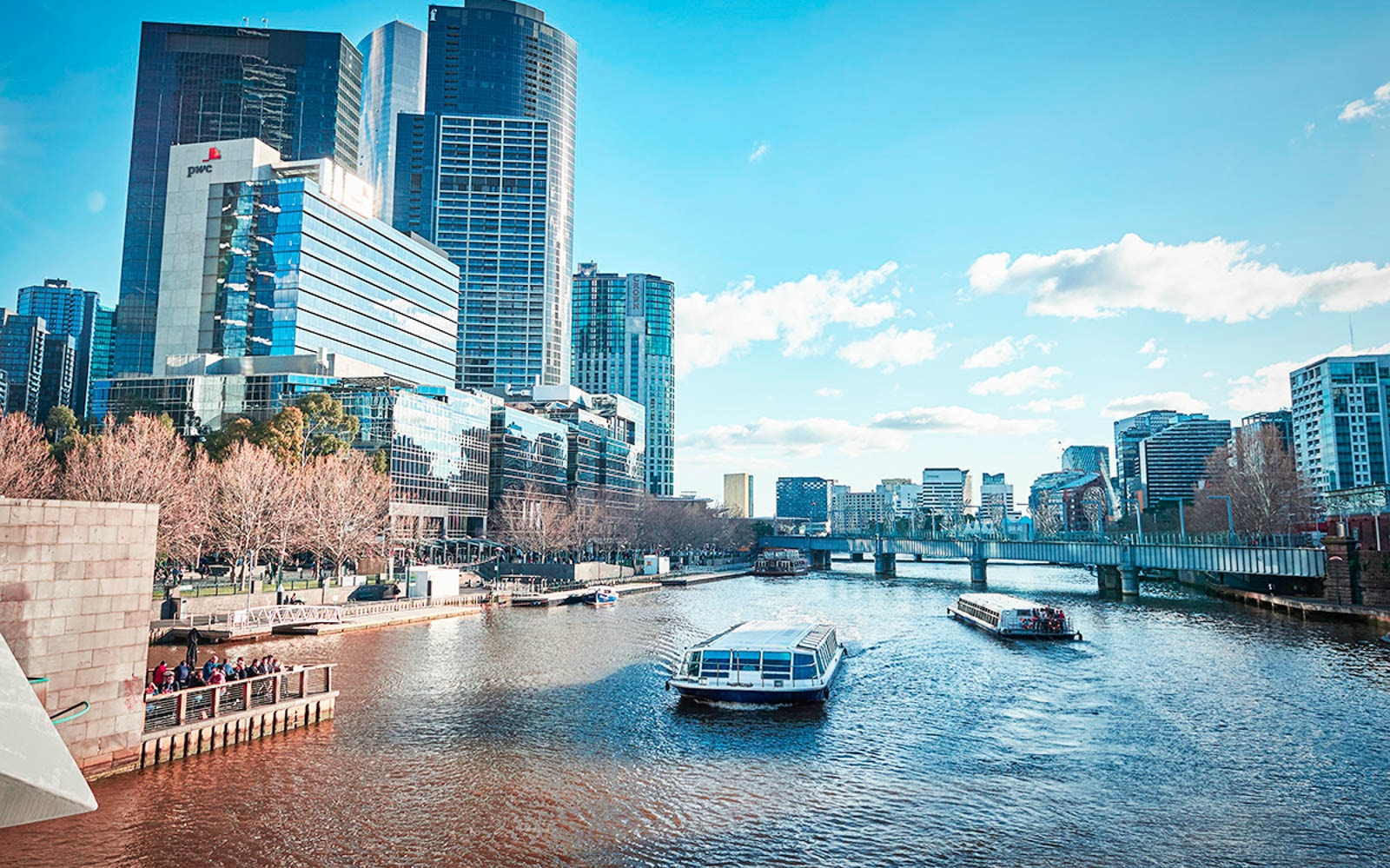 Melbourne river cruise passing under bridge with city skyline and docklands in view.