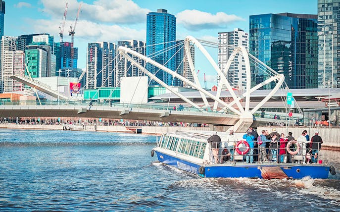 Tourists on a river cruise boat passing under a modern bridge in a cityscape.