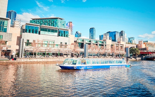 River cruise boat on Melbourne's Yarra River with cityscape backdrop.