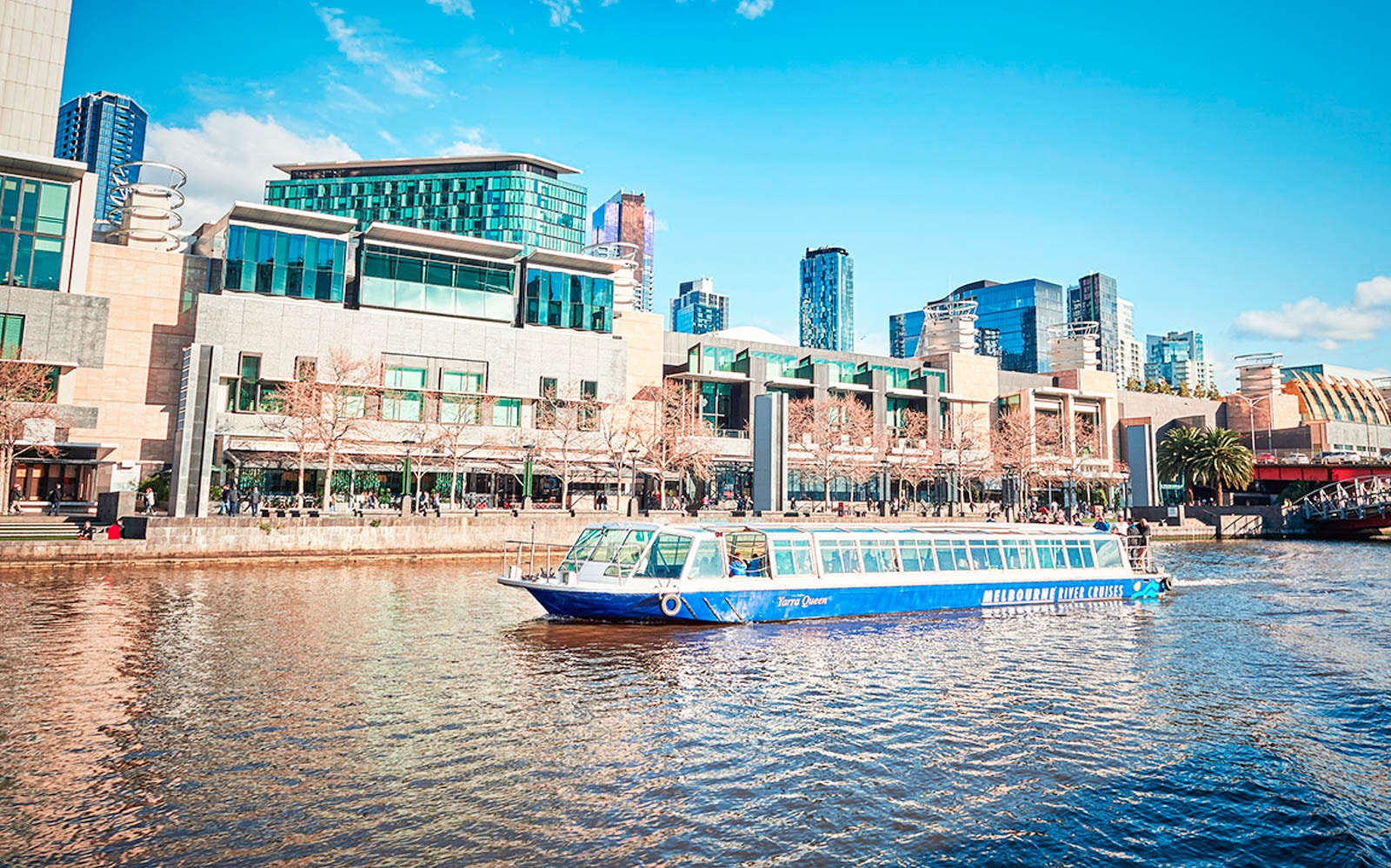 Melbourne river cruise boat passing lush gardens and city skyline.