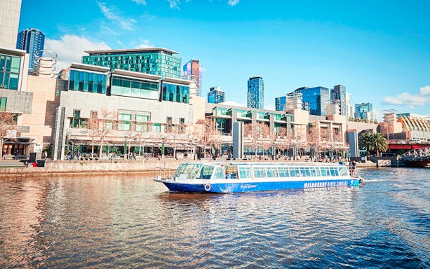 River cruise boat on Melbourne's Yarra River with cityscape backdrop.