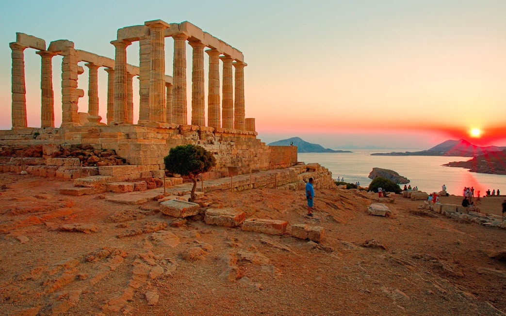 Temple of Poseidon at sunset, Cape Sounion, with tourists exploring the ancient ruins.