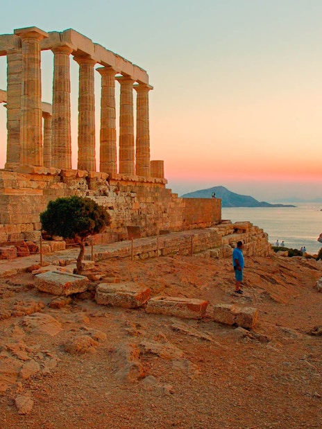 Temple of Poseidon at sunset, Cape Sounion, with tourists exploring the ancient ruins.