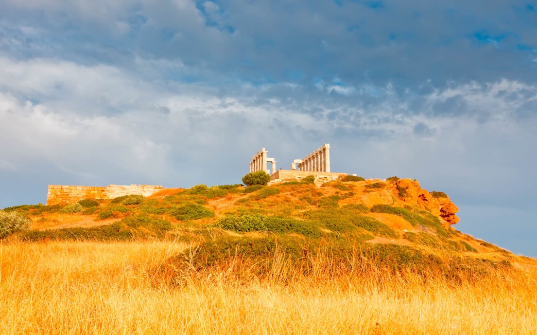 Temple of Poseidon on hilltop at Cape Sounion, Greece, with cloudy sky.