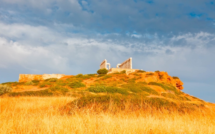 Temple of Poseidon on hilltop at Cape Sounion, Greece, with cloudy sky.