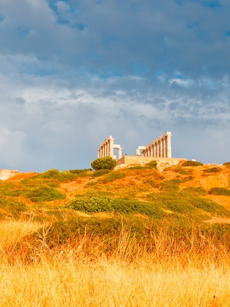 Temple of Poseidon on hilltop at Cape Sounion, Greece, with cloudy sky.