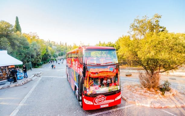 Hop-on-hop-off bus in Athens near lush greenery and tourists exploring.