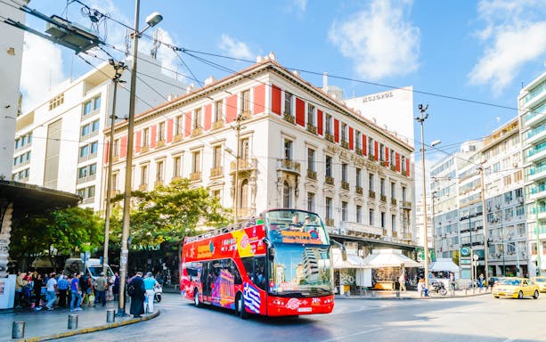 Red double-decker bus on Athens street, part of City Sightseeing tour, with historic buildings in the background.