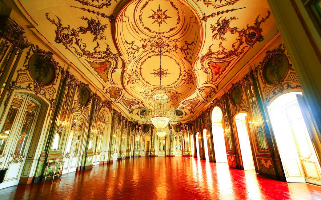 Ornate ballroom interior at the National Palace of Queluz, Portugal, featuring intricate ceiling designs and chandeliers.
