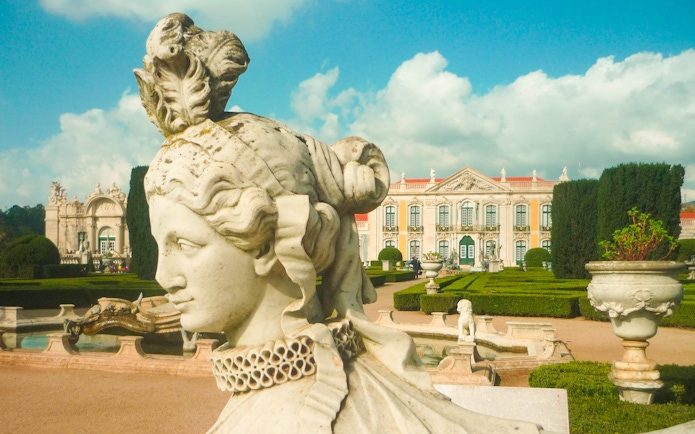 Statue in the gardens of the National Palace of Queluz, Portugal, with palace in background.