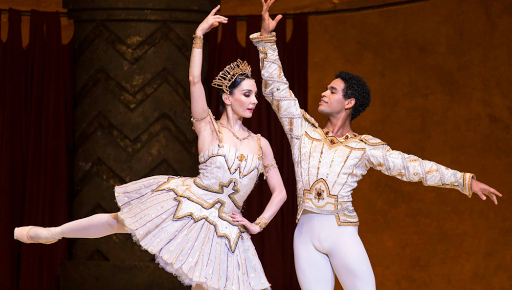 Ballet dancers performing Raymonda in ornate costumes on stage.
