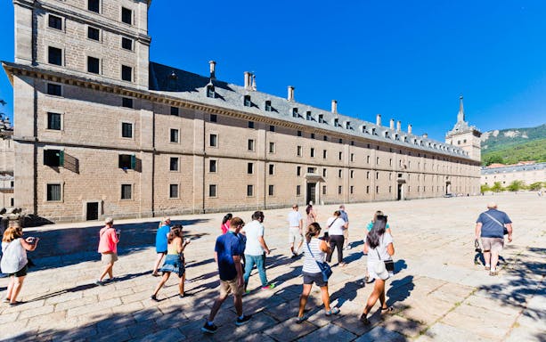 Tour group exploring the exterior of the Royal Monastery of El Escorial in Spain.
