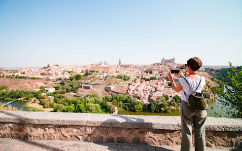 Person photographing Toledo cityscape from a viewpoint during guided tour.