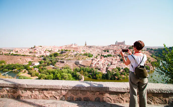 Person photographing Toledo cityscape from a viewpoint during guided tour.