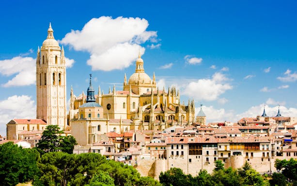 Segovia Cathedral with surrounding historic buildings under a blue sky.