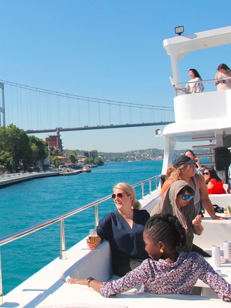 Bosphorus cruise with tourists enjoying lunch, Rumeli Fortress, and bridge in view.