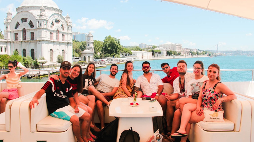 Group enjoying Bosphorus lunch cruise with view of Ortaköy Mosque and Bosphorus Bridge in Istanbul.