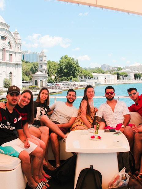 Group enjoying Bosphorus lunch cruise with view of Ortaköy Mosque and Bosphorus Bridge in Istanbul.