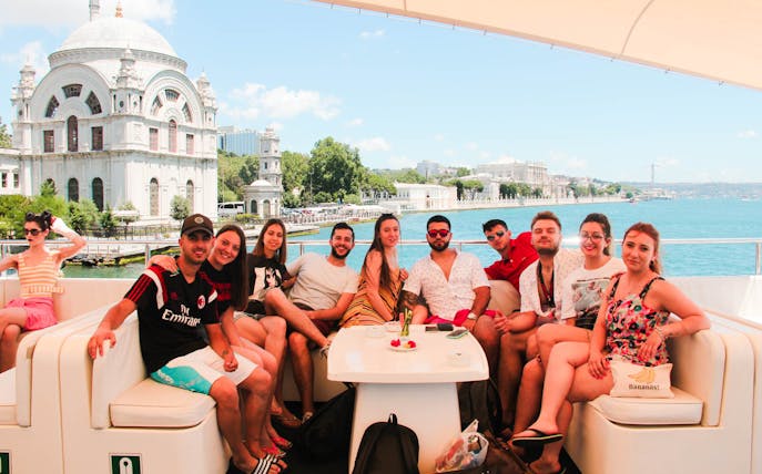 Group enjoying Bosphorus lunch cruise with view of Ortaköy Mosque and Bosphorus Bridge in Istanbul.