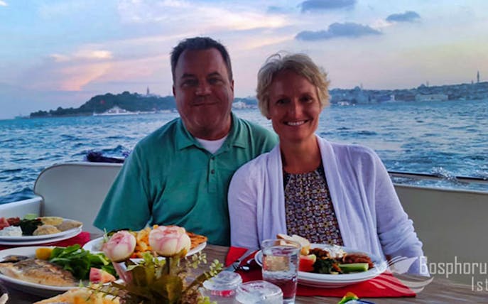 Couple dining on a Bosphorus cruise with Istanbul skyline in the background.