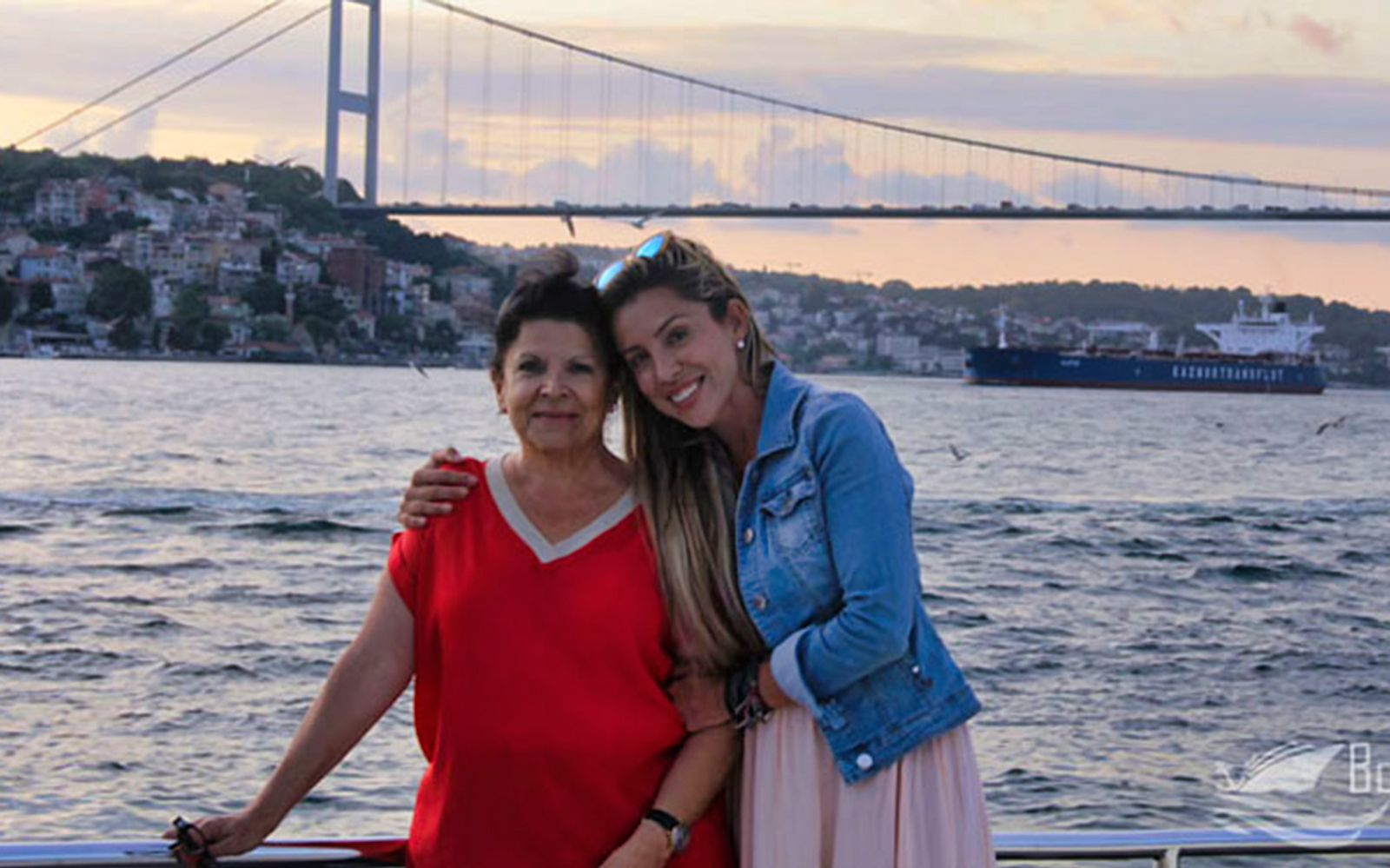 Two people on a boat with the Bosphorus Bridge in Istanbul in the background.