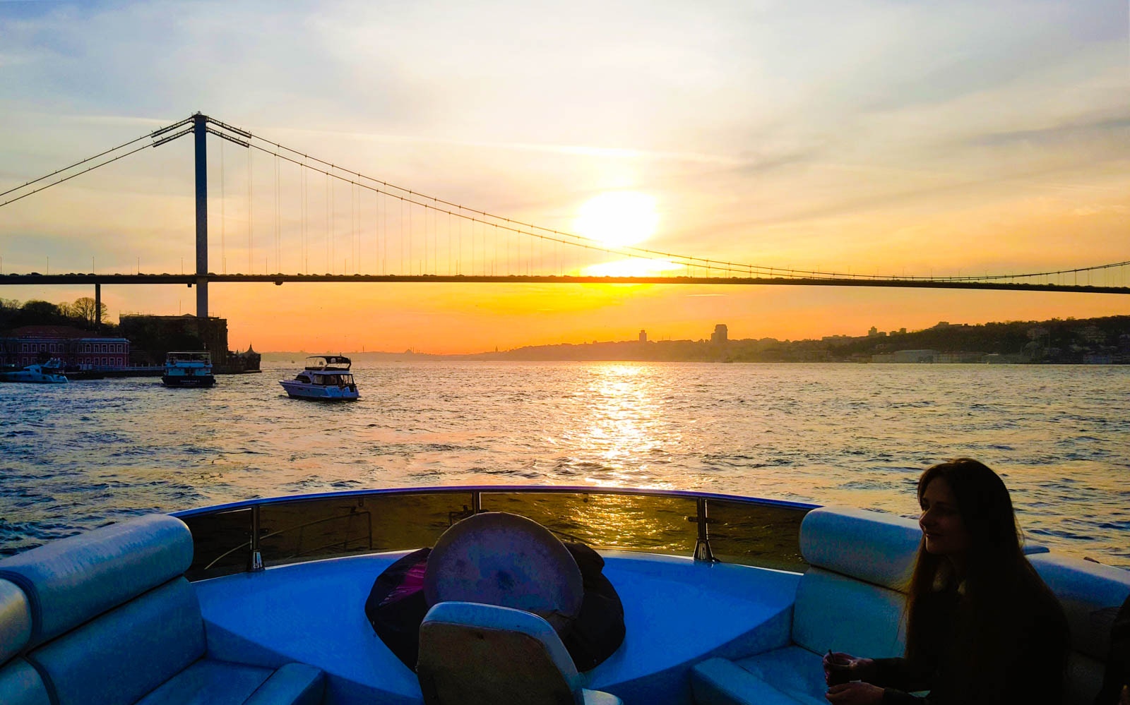 Bosphorus yacht cruise at sunset with guests enjoying drinks and canapés, Istanbul skyline in background.