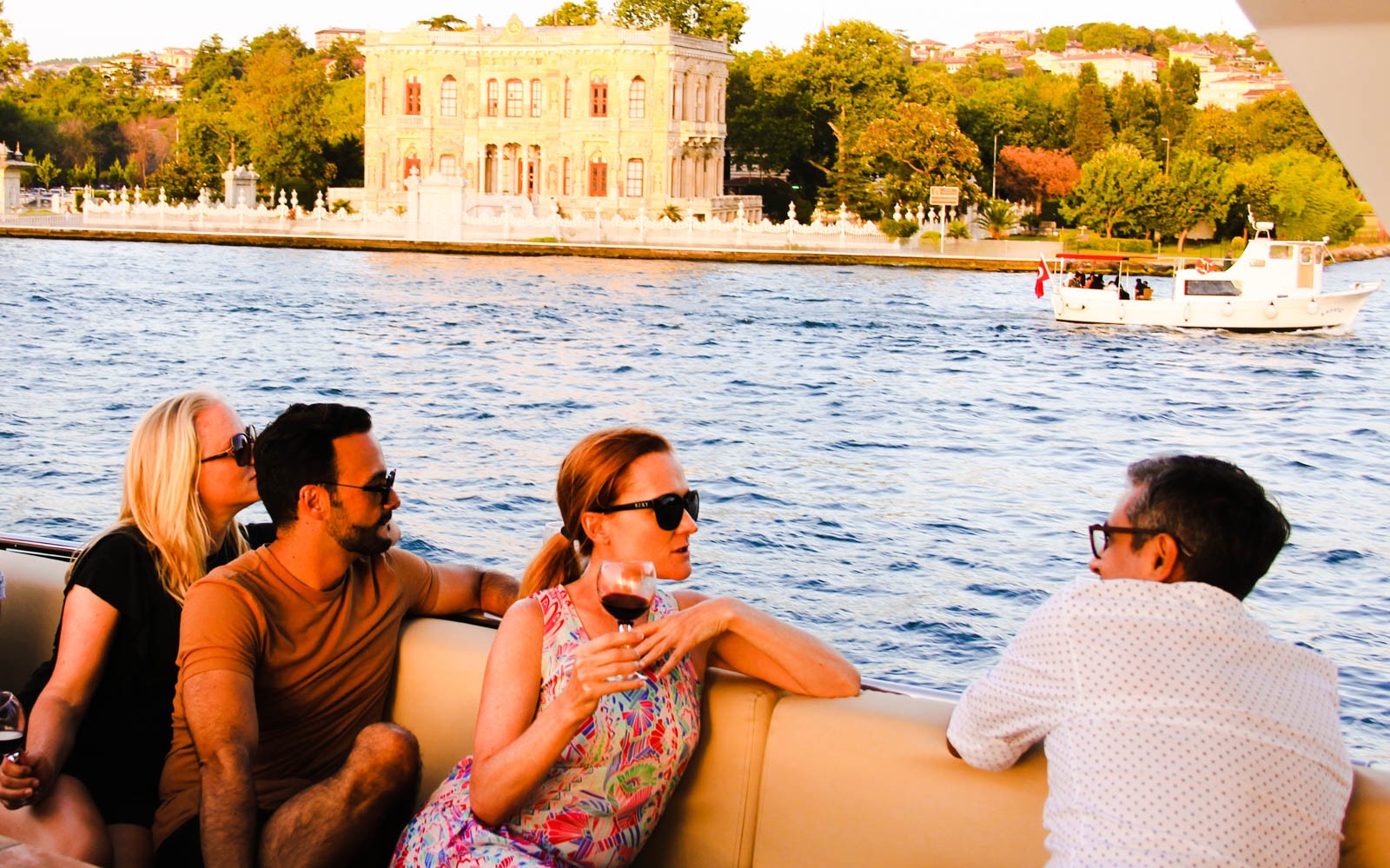 Bosphorus yacht cruise at sunset with guests enjoying drinks and canapes, Istanbul skyline in background.