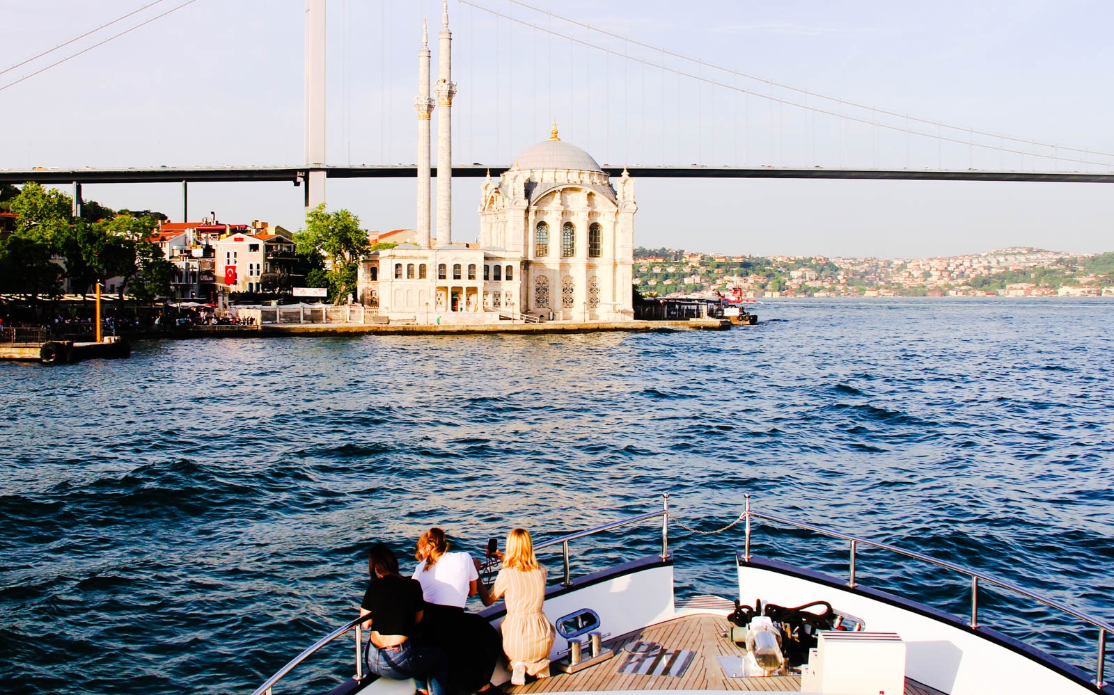 Bosphorus yacht cruise at sunset with guests enjoying drinks and canapés, Istanbul skyline in background.