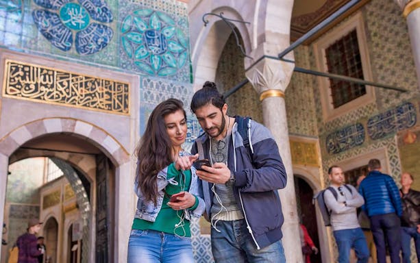 Visitors exploring Topkapi Palace entrance, Istanbul, with intricate tilework.