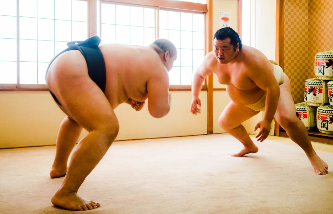 Sumo wrestlers preparing to engage in a match in a traditional Japanese setting.