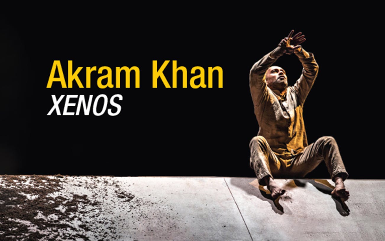 Dancer performing in Akram Khan's XENOS, seated on stage with arms raised.