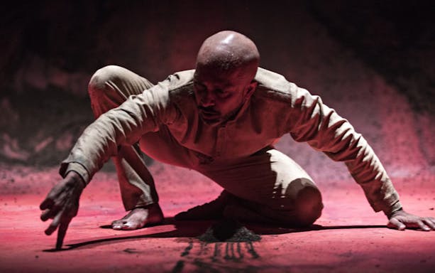 Performer crouching on stage during Akram Khan Company’s XENOS.