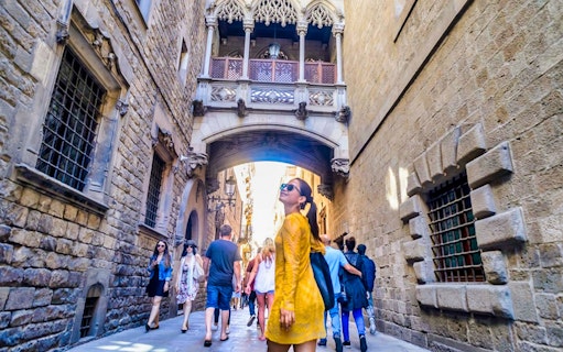 Gothic Quarter street with tourists walking under the Bridge of Sighs in Barcelona.