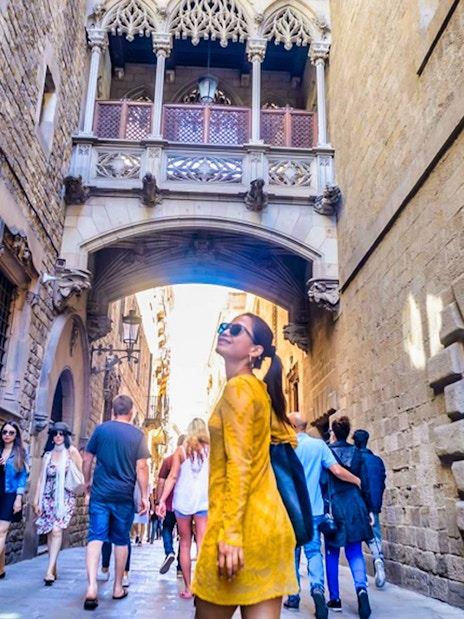 Gothic Quarter street with tourists walking under the Bridge of Sighs in Barcelona.