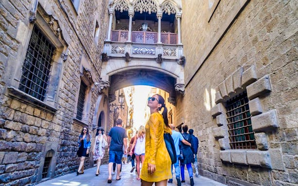 Gothic Quarter street with tourists walking under the Bridge of Sighs in Barcelona.