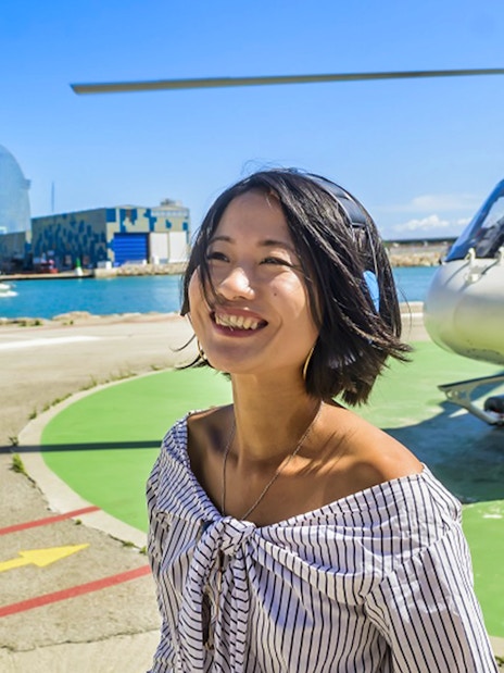 Smiling woman near helicopter with Barcelona skyline in the background.