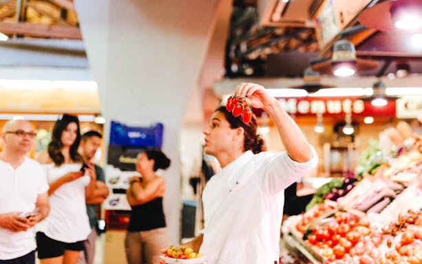 Local chef holding tomatoes during Barcelona market food tour.