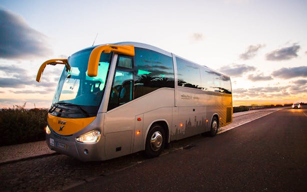 Tour bus parked on a road at sunset for Pena Palace & Sintra Half Day Tour from Lisbon.