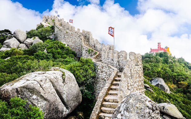Stone walls and steps of the Moorish Castle in Sintra with Pena Palace in the background.
